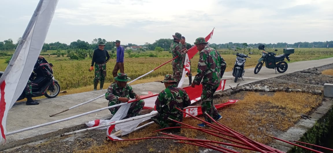 ANGGOTA SATGAS BERSAMA WARGA PASANG UMBUL UMBUL SAMBUT UPACARA TUTUP TMMD