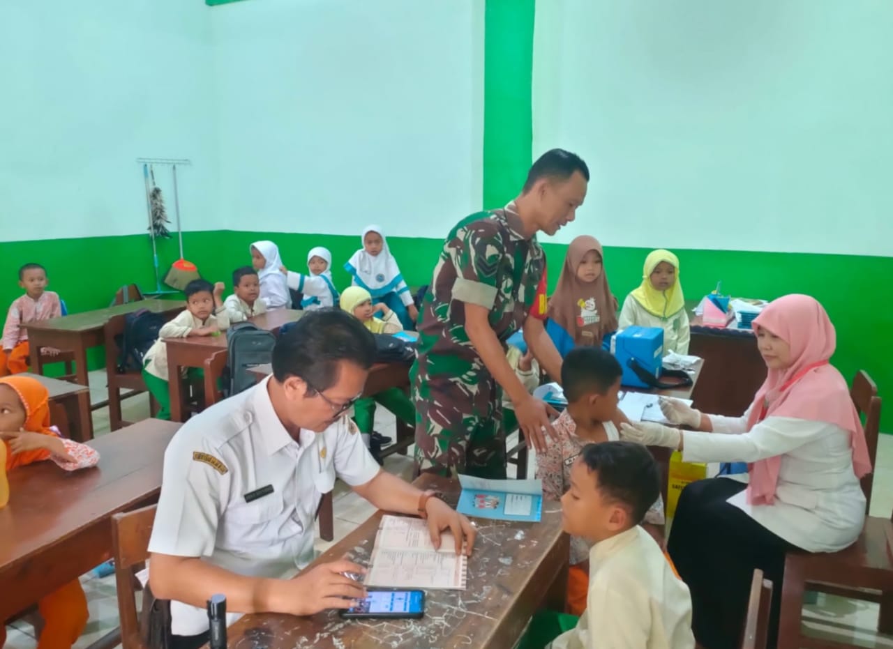 Sertu Marwan Seorang Babinsa yang Hangat dan Penuh Perhatian Membantu Menenangkan Anak-Anak Selama Bulan Imunisasi di Sekolah